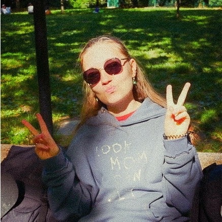 Tina sitting on a park bench in the sun, wearing sunglasses and showing peace signs with both hands